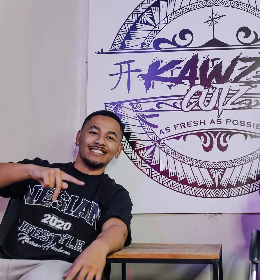 Kawza in the studio, seated in front of the Kawzacutz logo painted on the wall.