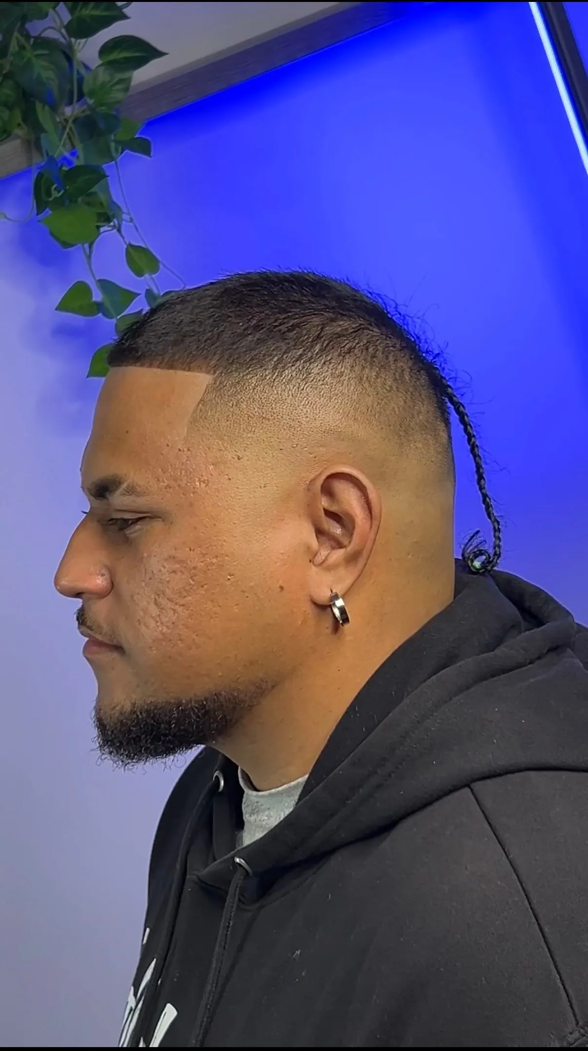Close buzz cut over a high skin fade, with a single braid left long at the back.