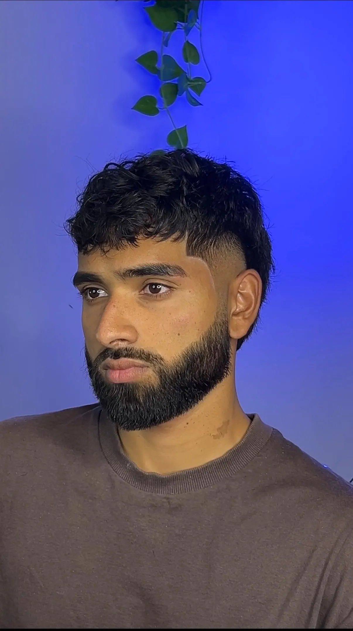 Curly fringe cut over a taper, finished with a full beard lined along the cheek.